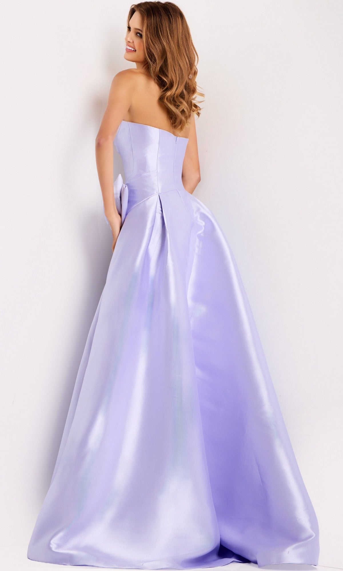 A woman in the Jovani 49196 Long Prom Dress, featuring a strapless satin bodice and A-line skirt, stands facing away and looks over her shoulder with a slight smile.